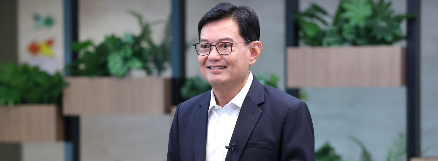 Person in suit and glasses with lavalier mic, backdrop with plants in wood planters.